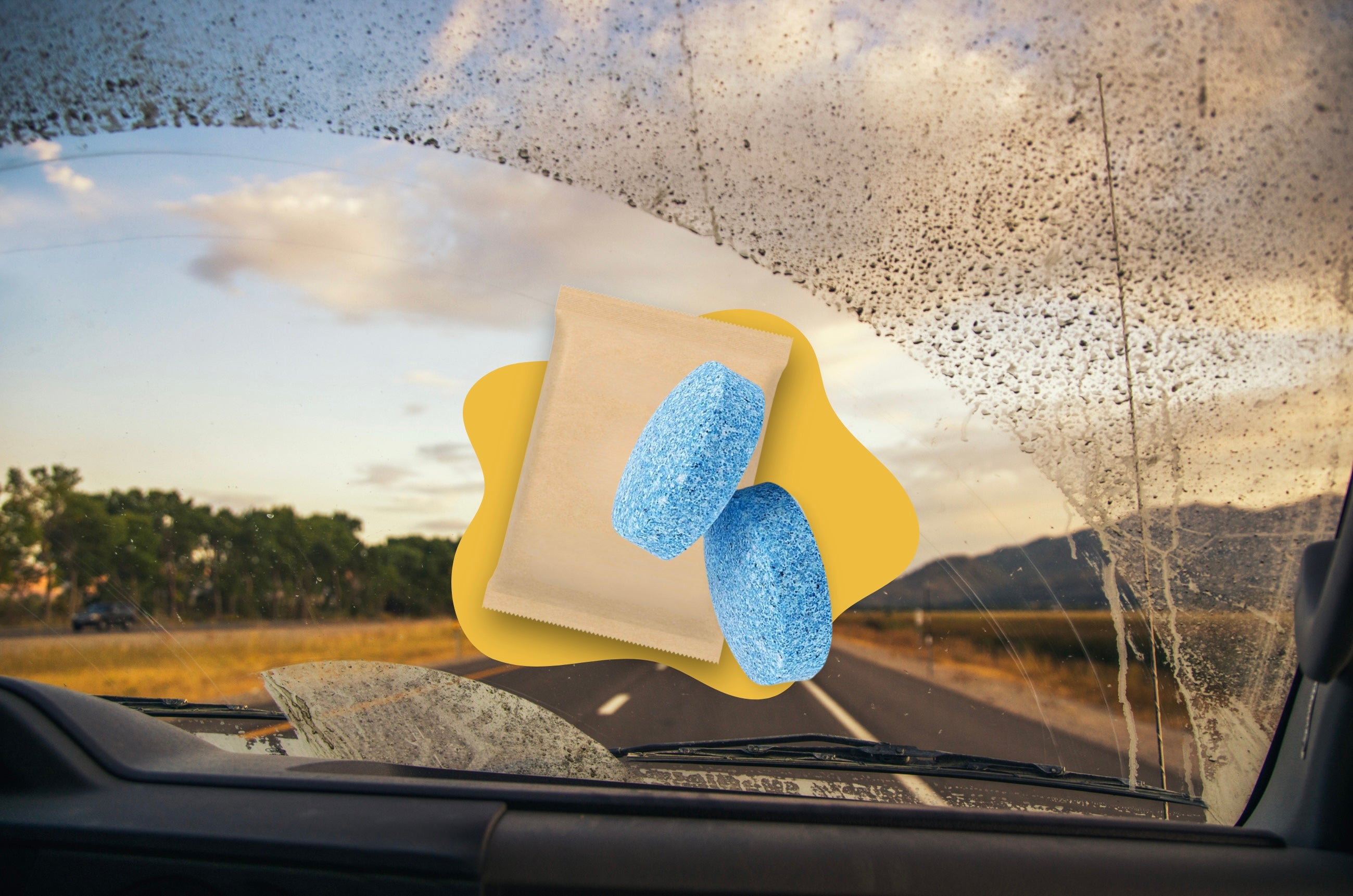 Two blue eco-friendly washer fluid tablets shown against a dirty car windshield on the road